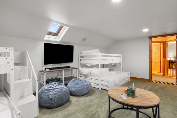 Two white twin-over-full bunk beds, a TV, and bean bag chairs under a skylight