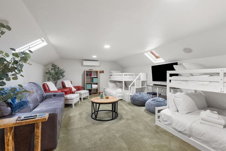 Bunk room with skylights, white bunk beds, a sofa, armchairs, bean bags, and a TV
