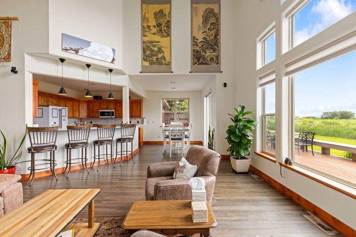 Open great room leading to the kitchen island with bar stools and a casual dining table, with windows onto the deck