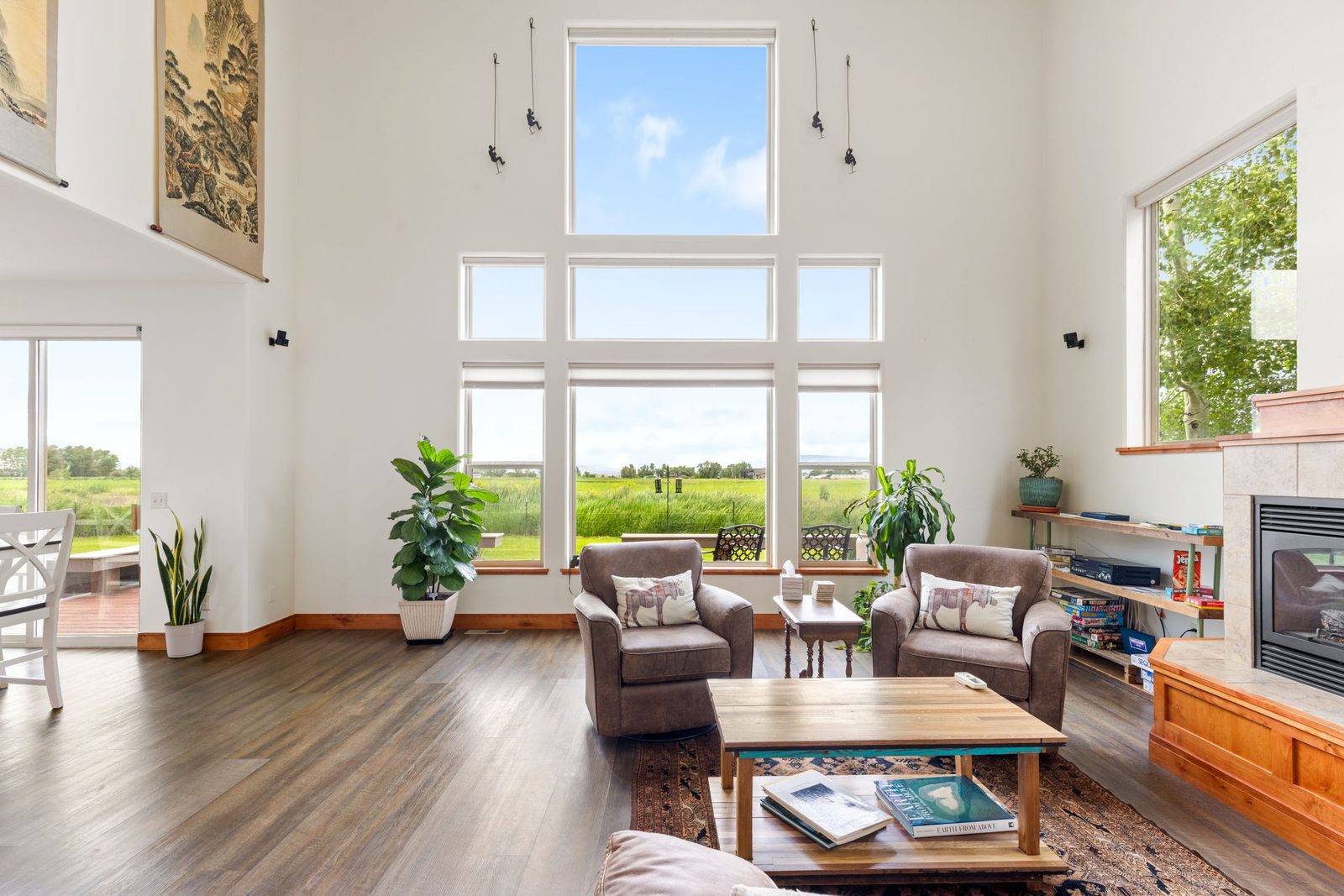 Great room with a two-story wall of windows looking out over open fields, armchairs, and a fireplace