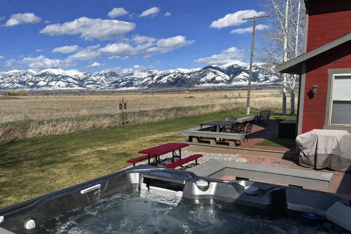Hot tub on the patio with picnic tables and the snow-capped Bridger Mountains across an open field