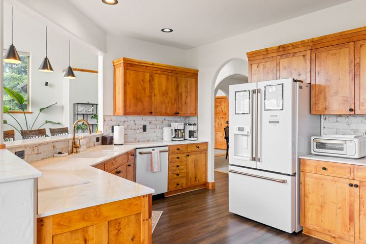Kitchen with knotty-alder cabinets, light stone countertops, white appliances, and a peninsula