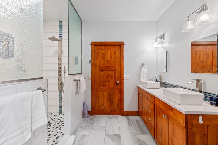 Primary bathroom with an oversized tiled walk-in shower, glass partition, and wood vanity