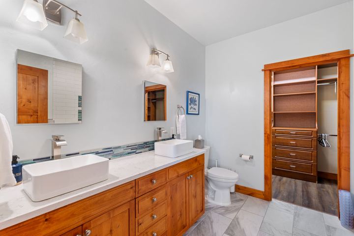 Primary bathroom with a double vanity, vessel sinks, and a doorway into a walk-in closet