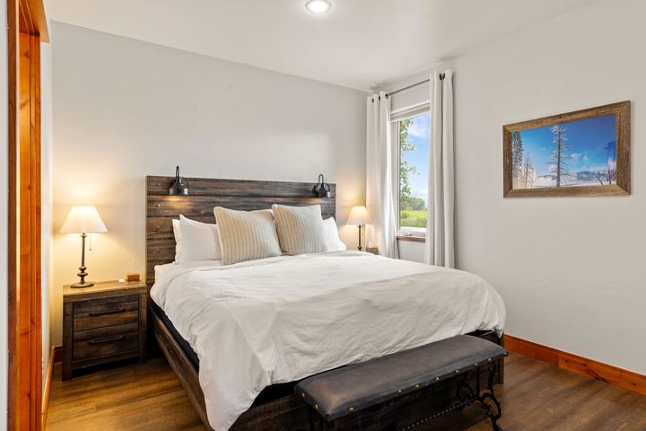Primary bedroom with a reclaimed-wood headboard, white bedding, bedside lamps, and a bench at the foot of the bed